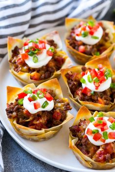 mini taco cups on a white plate topped with sour cream and toppings,