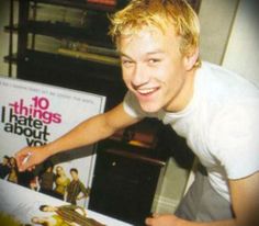 a young man smiles as he leans over a table in front of a poster for the movie 10 things i hate about you