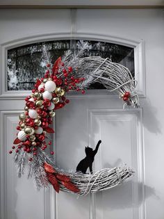 a cat is sitting in front of a door decorated with christmas decorations and balls on it