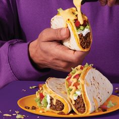 a person holding a burrito on a plate with other food items in front of them