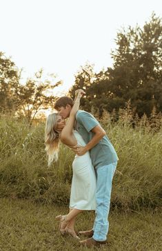 a man and woman kissing in the middle of tall grass with trees in the background