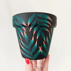 a woman's hand holding up a black and green cup with leaves on it