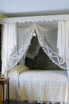 a white bed sitting in a bedroom next to a dresser and window with curtains on it