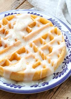 a blue and white plate topped with a waffle covered in icing on top of a wooden table