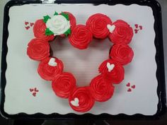 a heart shaped cake with red frosting and white roses on it's side