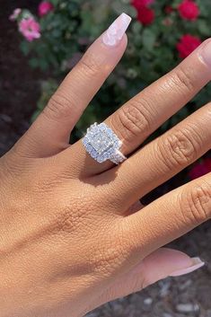 a woman's hand with a diamond ring on top of her finger and flowers in the background