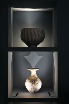 two black and white vases on display in a case with light coming from the top