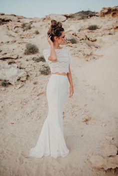 a woman standing on top of a sandy beach next to the ocean wearing a white dress