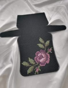 a cross stitched piece of cloth with a pink rose on it's side