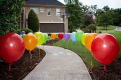 balloons are lined up on the sidewalk in front of a house with a driveway leading to it