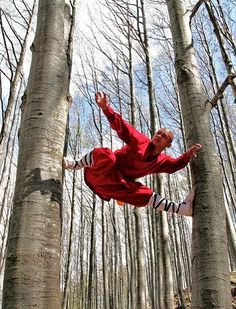 a man in red jumps up into the air between two trees