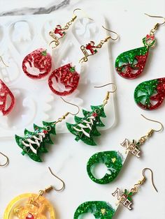 christmas themed earrings are displayed on a white surface, including one with green and red glitters