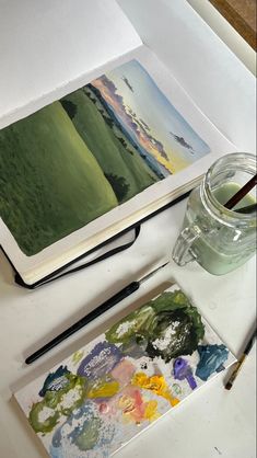 an artist's desk with paint, watercolors and a book on it