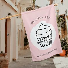 a pink banner with a cupcake on it hanging from a clothes line in an alleyway