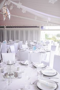 the tables are set for an event with white linens and snowflakes hanging from the ceiling