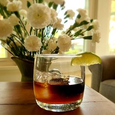 a glass filled with liquid and ice sitting on top of a table next to flowers