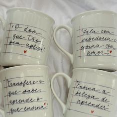 four coffee mugs with writing on them sitting next to each other in front of a white sheet