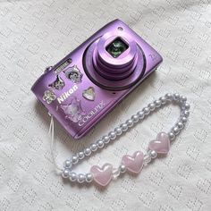 a purple camera sitting on top of a bed next to a beaded bracelet and necklace