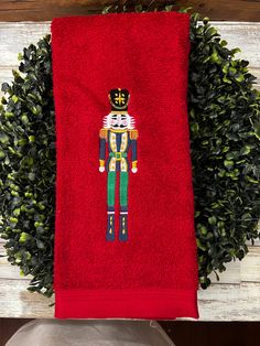 a red towel with a nutcracker embroidered on it sitting next to a potted plant