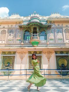 a woman standing in front of a building wearing a green dress and smiling at the camera