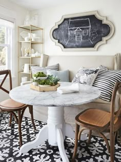 a table with two chairs and a chalkboard on the wall above it in a living room