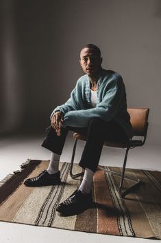 a man sitting in a chair on top of a rug with his legs crossed and feet crossed