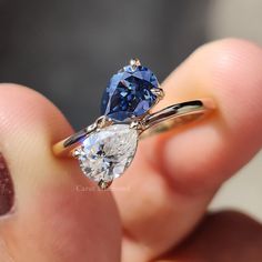 a person holding an engagement ring with two pear shaped diamonds