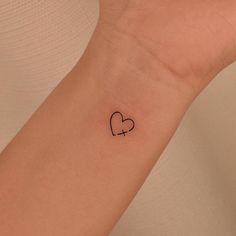 a small tattoo on the wrist of a woman with a heart and arrow in it