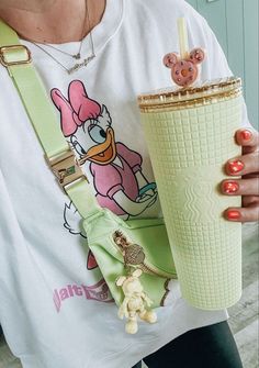 a woman holding a cup with a straw in her hand while wearing a mickey mouse t - shirt