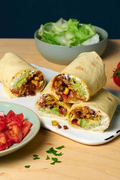 a burrito cut in half on a plate next to a bowl of lettuce and tomatoes