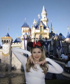 a woman posing in front of a castle with a minnie mouse ears on her head