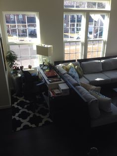 a living room filled with furniture and two large windows overlooking the parking lot in front of it