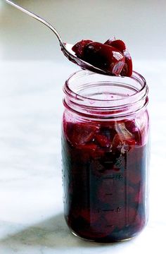 a spoon full of jam sitting on top of a white counter next to a jar