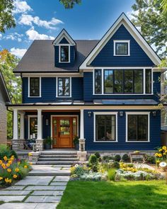 a large blue house with lots of windows and flowers in the front yard on a sunny day