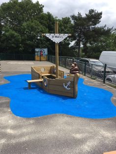 a pirate ship playground at the park with blue tarmac and trees in the background