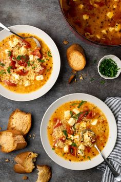 two white bowls filled with soup next to bread on a gray counter top and another bowl full of soup in the background