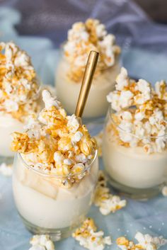 four small cups filled with popcorn on top of a blue cloth covered table next to silverware