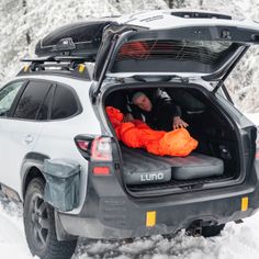 a man laying in the back of a car on top of snow covered ground