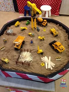 there is a large sand tray with construction vehicles in it and toys on the table