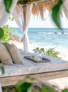 a bed on the beach with white sheets and pillows under a gazebo that overlooks the ocean