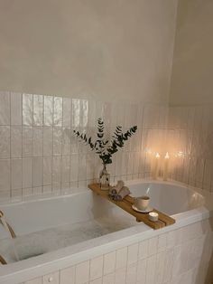 a white bath tub sitting inside of a bathroom next to a wooden tray filled with candles