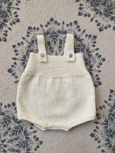 a white knitted baby romper with buttons on the front and bottom, sitting on a floral background