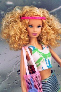 a barbie doll with blonde hair holding a pink bag and wearing a colorful outfit on the beach