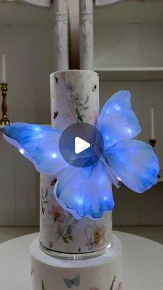 there is a blue butterfly on top of a white cake with candles in the background