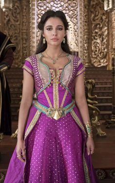 a woman in a purple dress with gold trims and jewels on her head, standing in