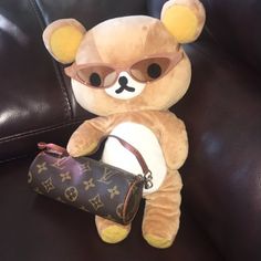 a brown teddy bear sitting on top of a couch holding a louis vuitton bag