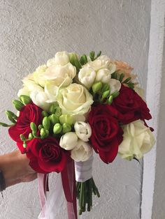 a bridal bouquet with red and white flowers in it is being held by someone's hand