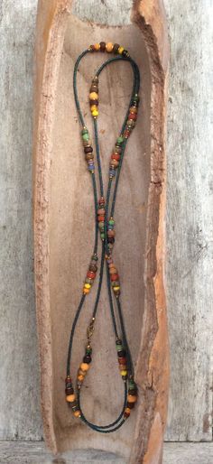 a long necklace with multicolored beads on a piece of driftwood in front of a wall