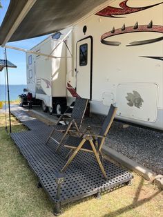 a camper with two chairs on the ground next to it