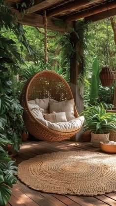 a hanging chair in the middle of a porch with potted plants and other greenery